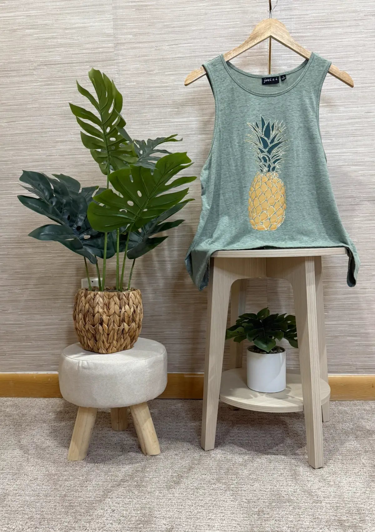Green tank top with pineapple design on a stool next to a plant