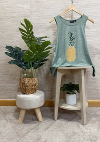 Green tank top with pineapple design on a stool next to a plant